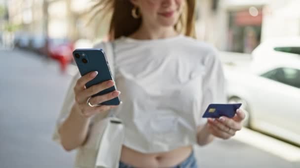 Mujer rubia joven de compras con teléfono inteligente y tarjeta de crédito en la calle - Imágenes, Vídeo