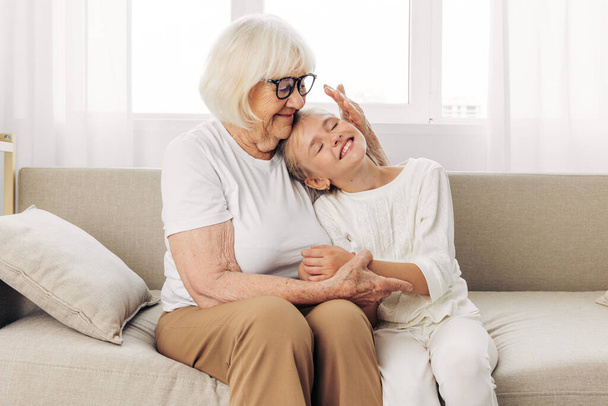 Стиль життя жінка дівчина зв'язує літня дочка обіймається сидячи онук додому бабуся стара сім'я старша мати щаслива любов бабуся диван диван генерація обійми - Фото, зображення