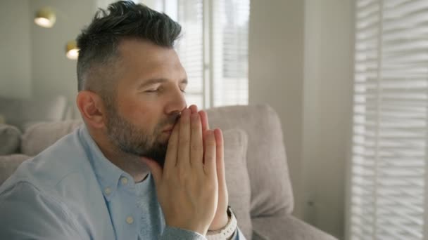 Grey haired male with beard puts hands in prayer praying with hope concept. Serious mature handsome man with stylish hairdo asking for help 4K. Man concerned about problem concentrating mind at home - Footage, Video