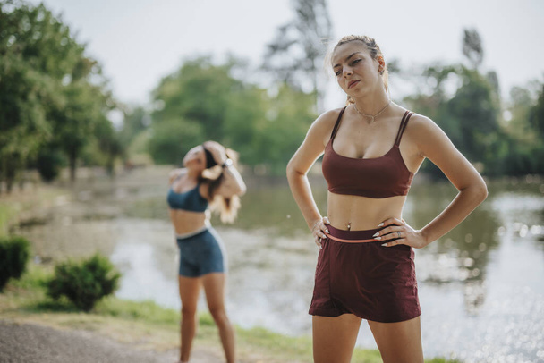 Donne atletiche in abbigliamento sportivo elegante esercizio all'aperto in un parco verde, allungando e flettendo i loro corpi in forma. - Foto, immagini
