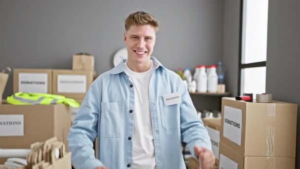Atraente, barbudo jovem caucasiano cara confiantemente voluntariado em um centro de caridade, sorrindo com polegares para cima gesto enquanto embalagem doações - Filmagem, Vídeo