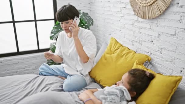 Liefdevolle moeder en dochter 's indoor medisch consult, ziek meisje verzorgd in de slaapkamer, geruststellend gesprek aan de telefoon met de dokter - Video
