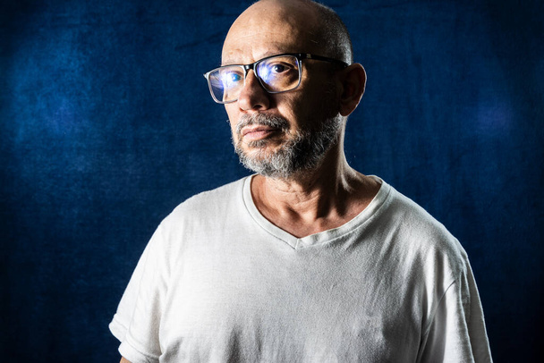 Man wearing glasses serious looking sadly against blue background. - Фото, изображение