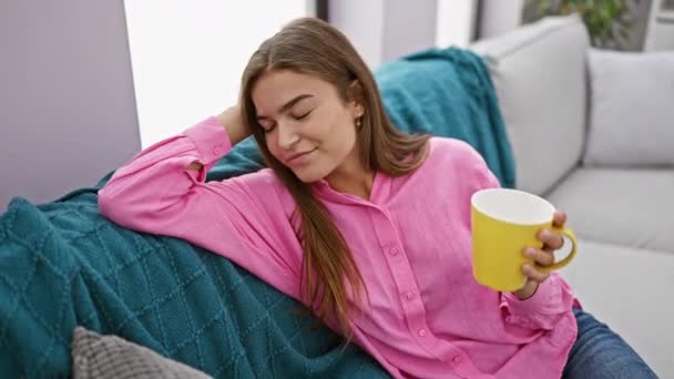 Νεαρή όμορφη ισπανίδα γυναίκα πίνει καφέ καθισμένη στον καναπέ στο σπίτι - Πλάνα, βίντεο