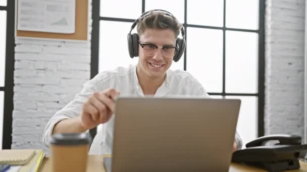 Переможний молодий кавказький чоловік святкує успіх бізнесу в офісі, виключаючи впевненість у ноутбуці та навушниках під час урочистості - Кадри, відео