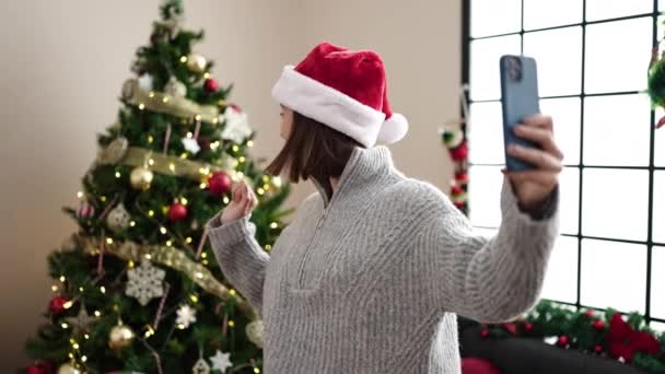 Молода красива іспаномовна жінка зі смартфоном, що посміхається впевнено стоїть на ялинці вдома - Кадри, відео