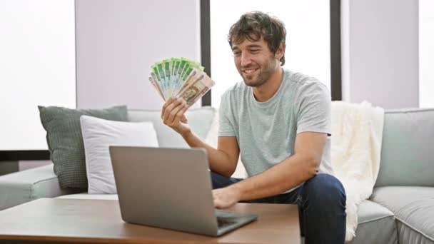Cheery, young man confidently approving with an ok sign, fingers gesturing the excellent symbol, whilst holding superior russian rubles, gleefully using his laptop at his home. - Footage, Video