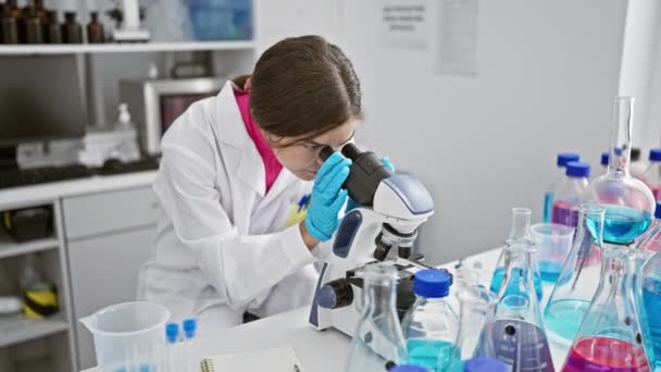 Zdenerwowana młoda Latynoska, piękna naukowiec, patrząc na mikroskop w laboratorium podczas pracy nad problemem w badaniach medycznych - Materiał filmowy, wideo