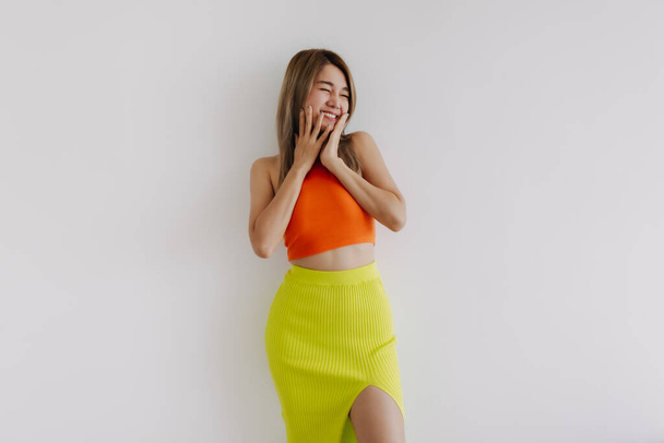 Happy cheerful cute asian woman in orange and green isolated on white. - 写真・画像