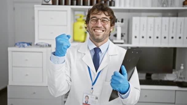 Захоплений молодий чоловік відзначає перемогу в лабораторії, з гордістю піднімає руку в тріумфальному успіху як блискучий вчений - Кадри, відео