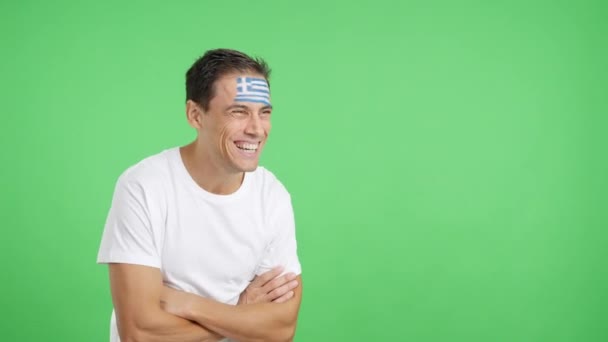 空白のコピースペースに顔を向けて描かれたギリシャの旗を持つ幸せな男のクロマとスタジオでのビデオ - 映像、動画