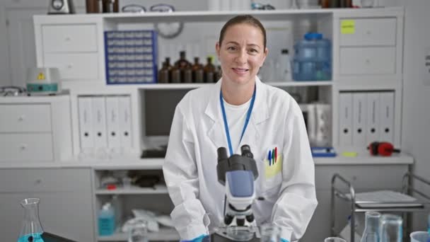 Radiosa giovane scienziata bionda, piena di fiducia, in piedi orgogliosa in laboratorio, il suo sorriso una testimonianza della gioia che si trova nella ricerca scientifica. - Filmati, video