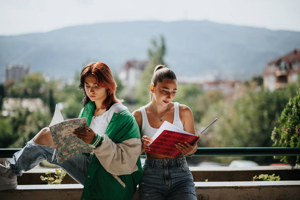 Dos mujeres jóvenes colaborando en un proyecto escolar al aire libre en la ciudad. Estudian juntos, preparándose para un examen y mostrando el trabajo en equipo y la amistad. - Foto, Imagen