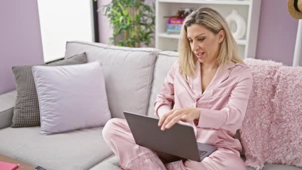 Mladá blondýna žena zavírání notebook ležící na pohovce sledování televize doma - Záběry, video