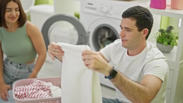 Schönes Paar lächelt zuversichtlich riechende saubere Kleidung in der Waschküche - Filmmaterial, Video