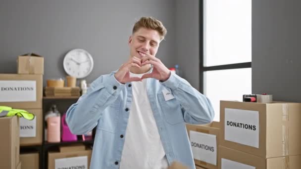 Красивий молодий кавказький чоловік наполегливо працює, впевнено волонтерюючи в серці громадського благодійного центру, його посмішка інфекційна, коли він стоїть насолоджуючись альтруїзмом, утворюючи прекрасний жест серця - Кадри, відео