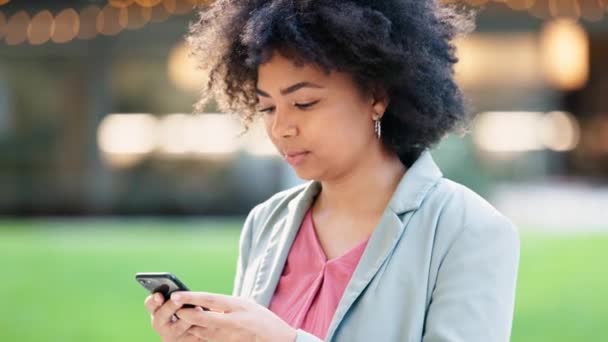 Happy fêmea navegando em um telefone on-line, enquanto está fora em um parque com bokeh. Mulher de negócios africana elegante com afro e terno digitar e-mails ou verificar as mídias sociais e olhar alegre. - Filmagem, Vídeo