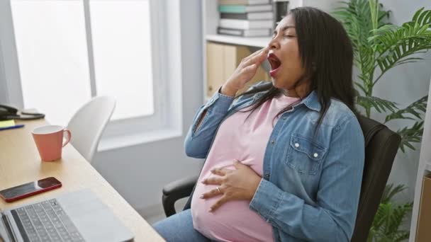 Exhausted young pregnant businesswoman yawning while touching her belly at the office, embodying maternity in the professional world. - Footage, Video