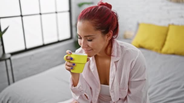 Ontspannen jonge roodharige vrouw genieten van het aroma van 's ochtends koffie terwijl comfortabel zitten in bed, binnen in haar gezellige slaapkamer - Video