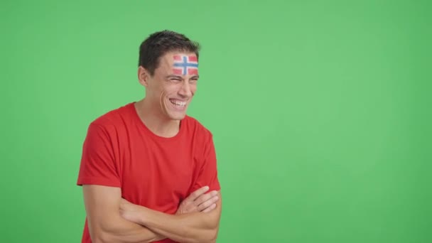 Video en estudio con croma de un hombre feliz con bandera noruega pintado en la cara mirando hacia el espacio de copia en blanco - Metraje, vídeo