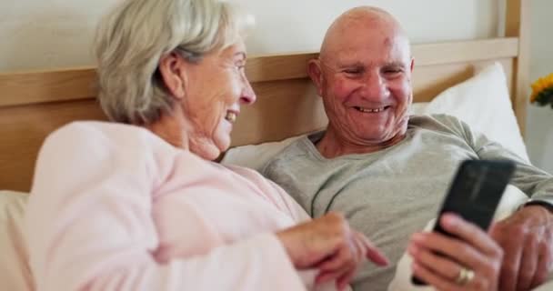Paar, samen en telefoon voor grappig op bed met sociale media, post of meme voor het lezen. Senior man, vrouw en tonen van boodschap, scroll en lees door internet, web of cel voor grap met de lach in band. - Video