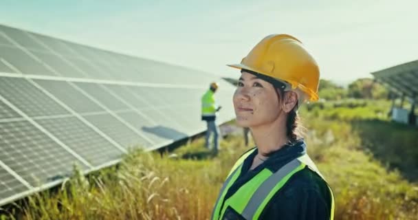 Женщина на ферме солнечных панелей для чистой энергии, наружного обслуживания электрической сети и улыбки. Устойчивость, фотоэлектрическая энергетическая система и счастливый техник со шлемом для проверки безопасности на заводе - Кадры, видео