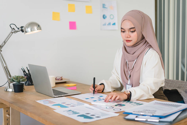 Junge muslimische Buchhalterin analysiert Geschäftsbericht am Arbeitsplatz - Foto, Bild