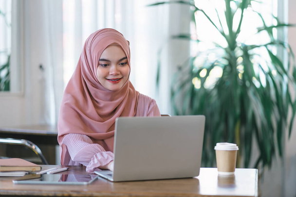 Milenyum Asyalı Müslüman serbest çalışan iş kadını bir kafede dizüstü bilgisayar kullanıyor. - Fotoğraf, Görsel
