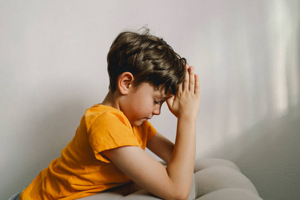 Ein Junge in orangefarbenem T-Shirt betet zu Hause. Die Bibel lesen. Konzept für Glauben, Spiritualität und Religion. Frieden, Hoffnung. - Foto, Bild
