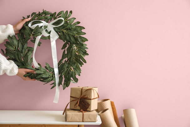 Mãos femininas com grinalda de Natal e presentes na mesa perto da parede rosa. Banner para design - Foto, Imagem