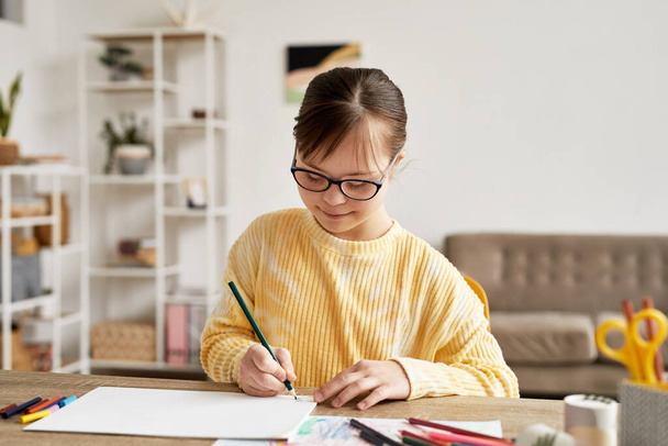 Portrait d'une adolescente trisomique dessinant des images à table dans une pièce confortable et souriante, espace de copie - Photo, image