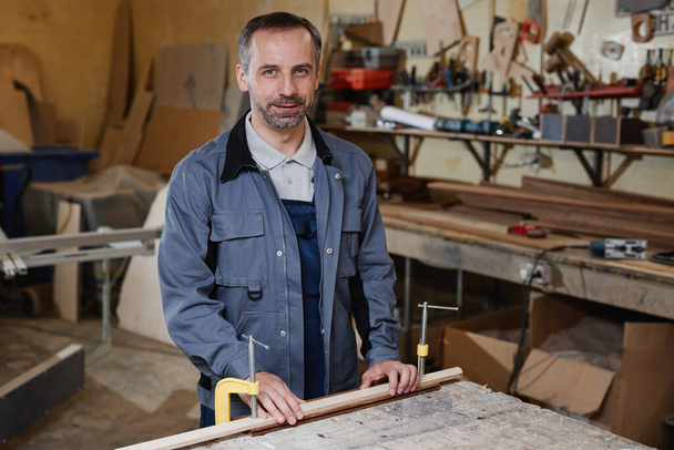 Portrait taille haute d'un travailleur masculin mature regardant la caméra tout en travaillant avec du bois dans un atelier d'usine, espace de copie - Photo, image