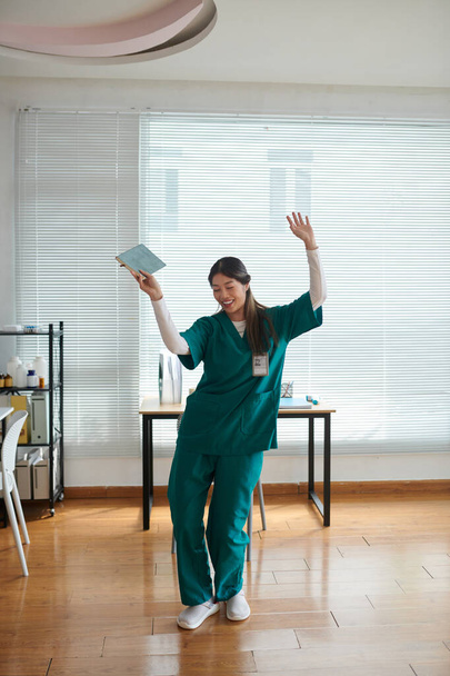 Medische verpleegkundige in groene scrubs dansen in het ziekenhuis lounge na het beëindigen van de dienst - Foto, afbeelding