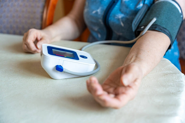 Starší žena doma kontroluje hladinu krevního tlaku, starší žena trpí vysokým krevním tlakem, sedí a používá pulzometr, tonometr. Kvalitní fotografie - Fotografie, Obrázek