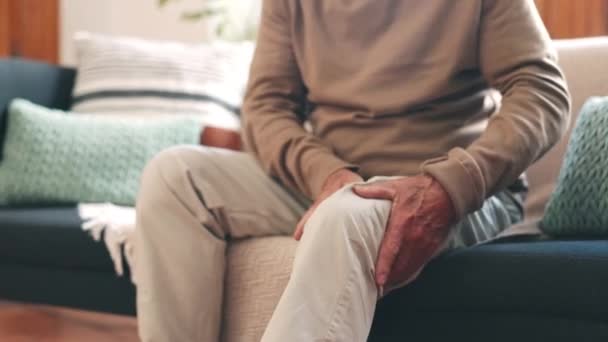 Manos, dolor de rodilla u osteoporosis con una persona mayor en un sofá en el salón de su casa de cerca. Masaje, pierna o anatomía y un adulto mayor con una lesión articular, fibromialgia o inflamación. - Metraje, vídeo