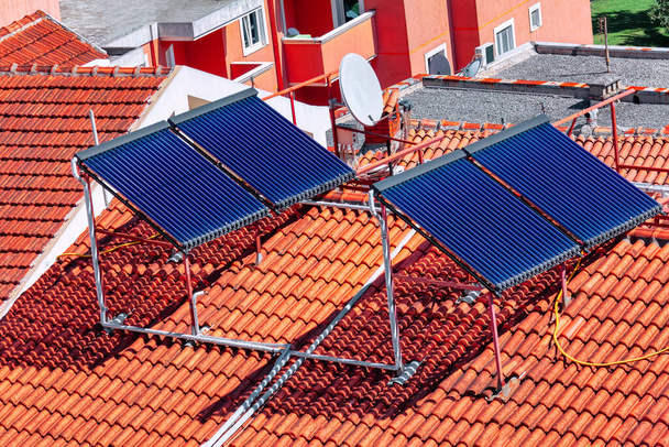 Çatıdaki ısıtma suyu için güneş enerjisi toplayıcıları. Güneş kolleksiyoncuları kiremitli çatıyı süsleyerek, suyu ısıtmak için çevre dostu bir elektrik santraline dönüştürüyorlar. - Fotoğraf, Görsel