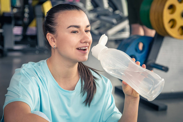 Woman with a bottle of water in the gym after a workout, lifestyle bodybuilding. - Photo, Image