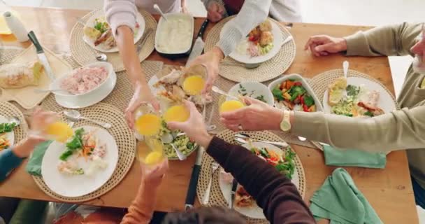 Ebéd, éljenzés és család gyümölcslével az ebédlőben az egészség, wellness és táplálkozási ételekhez. Pirítós, ünneplés és felső nézet közelkép az emberek gyümölcs ital egy villásreggeli vagy reggeli esemény otthon - Felvétel, videó