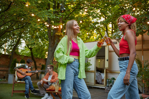 Wenig betrunken zwei Jahrtausendweiber, die sich umarmen und miteinander tanzen. Junge Erwachsene genießen unbeschwerte Zeit auf dem Campingplatz im Urlaub. Picknick im Freien mit Freunden - Foto, Bild