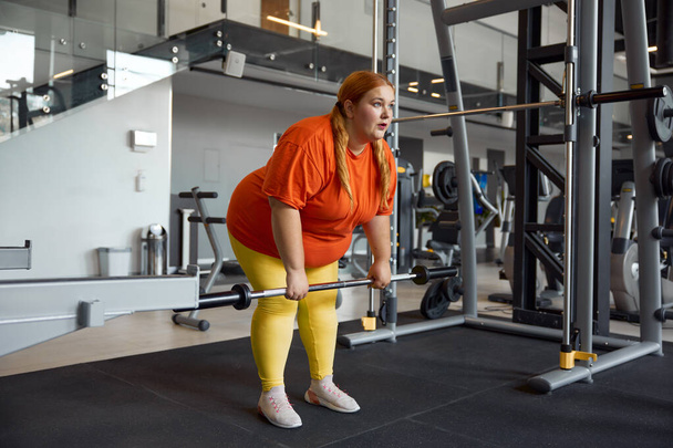 Молода жінка з надмірною вагою тренується з штанговим рядком для втрати ваги і перекачування сили. Персональна спортивна підготовка в спортзалі - Фото, зображення