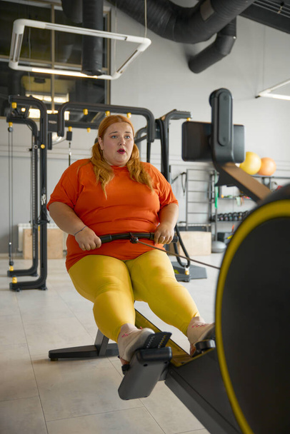 Donna paffuta che lavora sodo sulla macchina da allenamento in palestra. Obesità lotta e concetto di sport - Foto, immagini