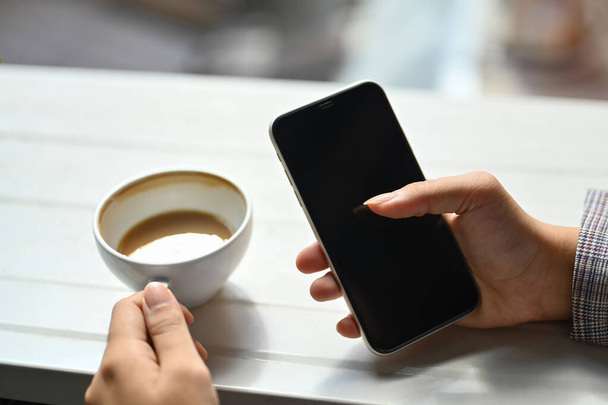 Vista de cerca mujer mano sosteniendo la taza de café y teléfono inteligente. - Foto, Imagen