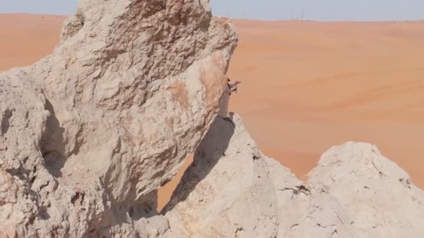 Um drone voa em torno de um homem barbudo vestido como um xamã que ora em um penhasco no deserto arenoso dos Emirados Árabes Unidos. Vista aérea - Filmagem, Vídeo