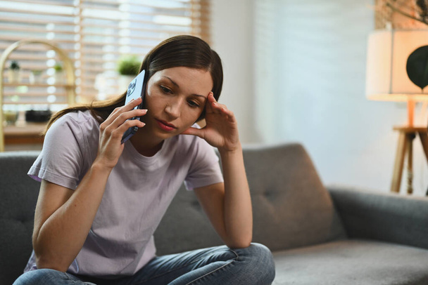 Zamartwiona młoda kobieta rozmawia przez telefon otrzymując złe wieści i czując się zdesperowana. - Zdjęcie, obraz