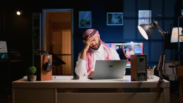 Κουρασμένος Άραβας επιχειρηματίας που υποφέρει από ημικρανία δουλεύοντας στο γραφείο του σπιτιού. Εξαντλημένος εργαζόμενος της Μέσης Ανατολής στο σαλόνι απαντώντας σε μηνύματα ηλεκτρονικού ταχυδρομείου πάρει πονοκέφαλο από την υπερεργασία - Πλάνα, βίντεο