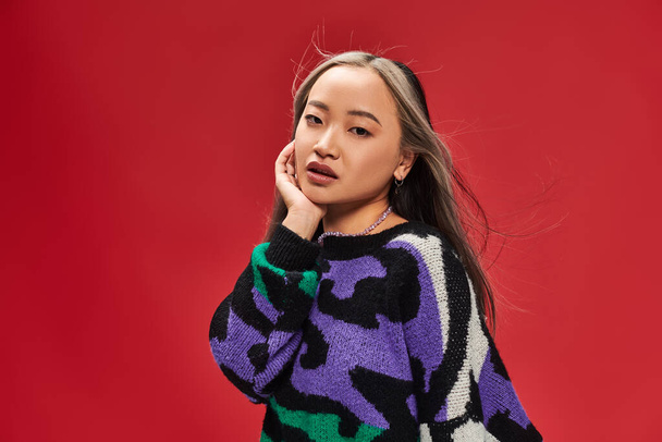 hermosa joven asiático mujer con teñido pelo en suéter con animal print posando con mano cerca de cara - Foto, Imagen