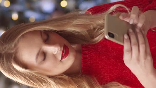 Muotokuva blondi valkoihoinen nainen punaisella huulipunalla aktiivisesti viestien ystäviensä tai poikaystävänsä puhelimessa. Nuori nainen kommunikoi sosiaalisessa mediassa. Positiivisesti hymyilee käyttäessään hänen gadget. - Materiaali, video