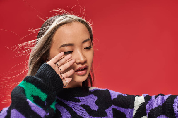 young asian woman with dyed hair in sweater with animal print posing with hand near face, wind - Photo, Image