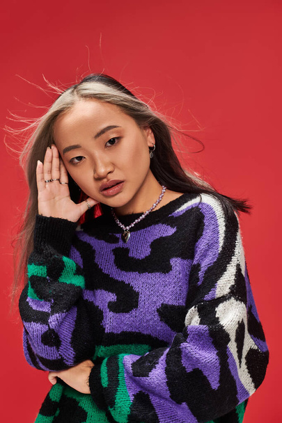 alluring young asian woman with dyed hair in sweater with animal print posing with hand near face - Photo, Image