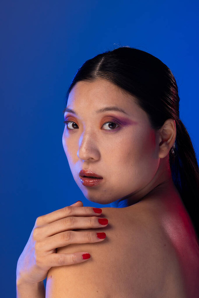 Portrait of asian woman with black hair wearing purple eye shadow on blue background. Cosmetics, makeup, female fashion and beauty, unaltered. - Fotoğraf, Görsel